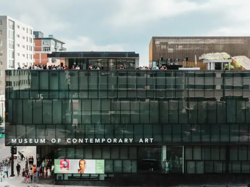 People gather on the rooftop of the Museum of Contemporary Art Denver, enjoying the city views. Photos of the museum showcase its modern architecture.