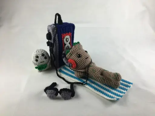 Amigurumi Baby Groot tumbado con auriculares junto a un reproductor de música y un pequeño personaje gris.