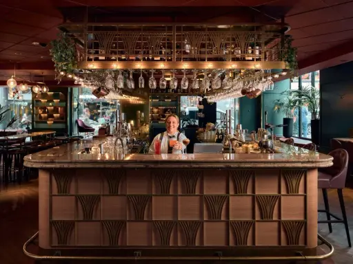 En glad bartender vid en elegant cocktail bar i Stockholm, med drinkar och glas på rad.