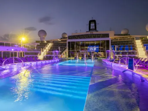 Piscine illuminate con luci viola e blu sulla MSC World Europa, con sdraio e scale illuminate.