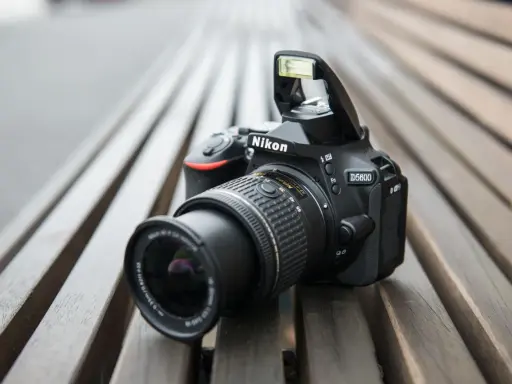 Czarny aparat Nikon D5600 z wysuniętą lampą błyskową leży na drewnianej ławce. Idealny do nikon d5600 test.