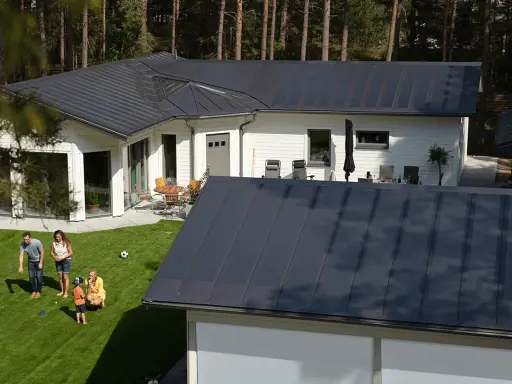 Familj njuter av solen på gräsmattan framför ett modernt hus med ett stilrent lindab solar roof.
