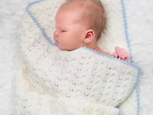 Sover sött i en stickad filt. Att knyta sjal bebis är ett mysigt sätt att hålla dem varma.