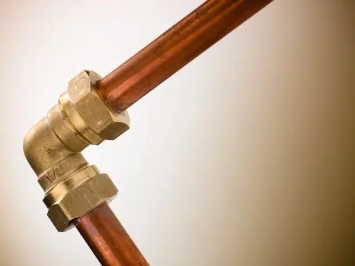 Un raccord coudé en laiton relie deux tuyaux en cuivre, illustrant une plomberie sans soudure efficace et durable.