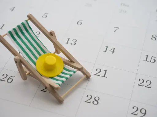 Miniaturowa leżanka plażowa z zielono-białymi pasami i żółtym kapeluszem na tle kalendarza.