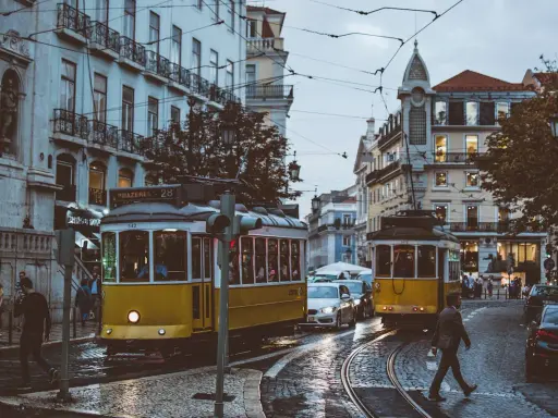 Lisbona, Portugalia. Żółte tramwaje na brukowanej ulicy, ludzie i samochody. Ceny w Portugalii mogą być różne, ale widok wart jest każdej ceny.