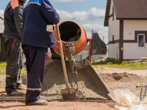 Robotnicy mieszają beton. Widać, ile piasku na worek cementu potrzeba do uzyskania odpowiedniej konsystencji.