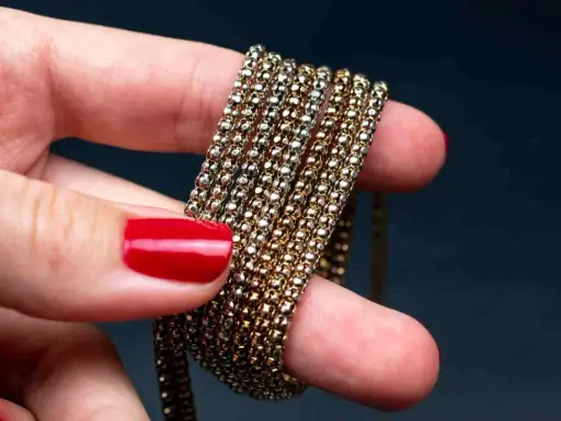 Main d'une femme aux ongles rouges tenant une chaîne de métal doré, montrant comment nettoyer métal doré noirci.