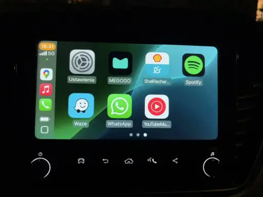 Ekran samochodu z ikonami aplikacji: Ustawienia, MEGOGO, Shell Recharge, Spotify, Waze, WhatsApp, YouTube Music. Działa system iOS CarPlay.