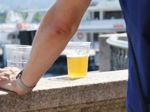 Ręka opiera się o kamienny murek, obok piwo w plastiku. Może to początek drogi do spadku wagi po odstawieniu piwa.