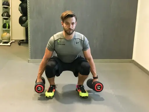 Mann macht Kniebeugen mit Kurzhanteln. Er hält zwei Hanteln mit je 14 kg Gewicht.
