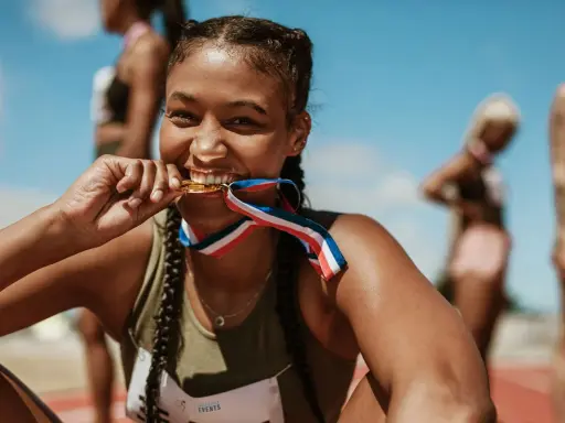 Läuferin beißt stolz in ihre Goldmedaille. Ihr Trainingsplan Laufen 10 km hat sich ausgezahlt.