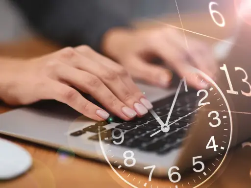 Dłonie piszą na klawiaturze laptopa, a nad nimi unosi się zegar. 0440 znaczenie czasu w pracy.