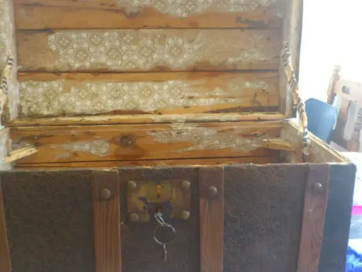 Baúl antiguo con chapa de latón oxidada y desgastada, listo para restaurar. El interior muestra restos de papel pintado.