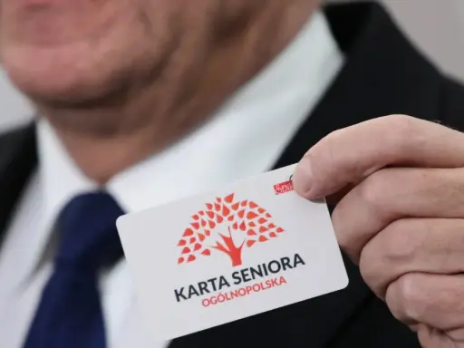 Dłoń trzyma białą kartę z czerwonym drzewem i napisem "KARTA SENIORA OGÓLNOPOLSKA".