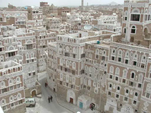 Ein malerisches arabisches Haus mit kunstvollen weißen Verzierungen und vielen Fenstern, eingebettet in eine Stadt mit ähnlicher Architektur.