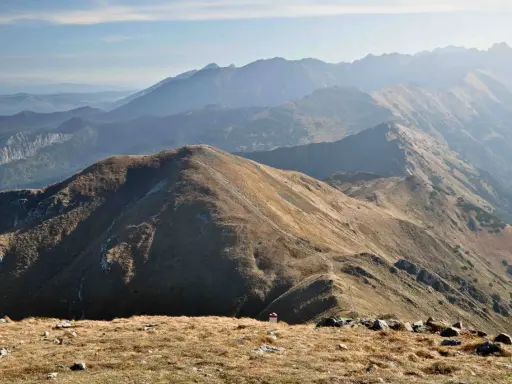 Widok na pasmo górskie Tatr. W oddali widać kolejne grzbiety górskie, a na pierwszym planie ścieżki i kamienie. Trasy Tatry zachęcają do wędrówki.