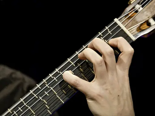 Main d'un guitariste jouant sur une microtonal guitar, ses doigts effleurant les cordes sur un manche sombre.