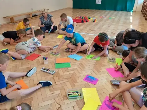 Dzieci biorą udział w zabawach animacyjnych, rysując na kolorowych kartkach.