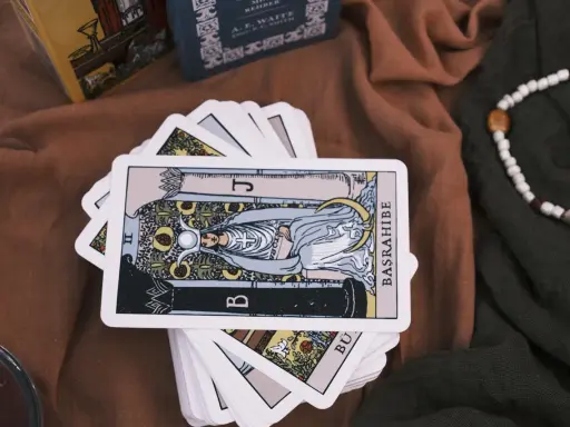 Karty tarota ułożone na brązowym materiale. Jedna karta, przedstawiająca postać z księżycem i owocami, jest na wierzchu. To idealny obrazek na **tarot na tydzień**.