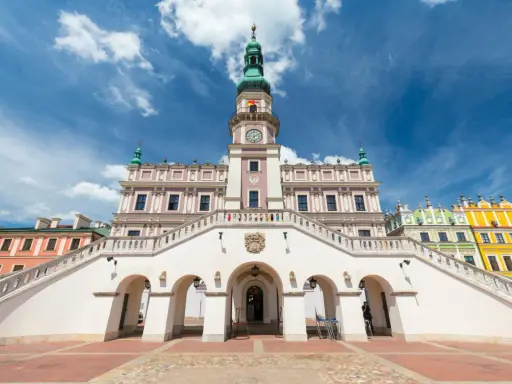 Zamość rynek: Ratusz z imponującymi schodami i kolorowe kamienice pod błękitnym niebem.