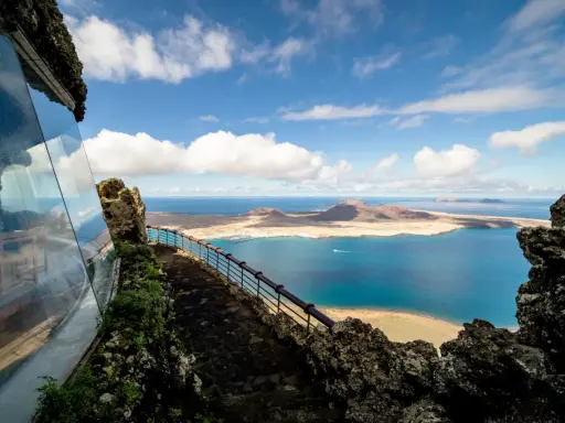 Blick vom Mirador del Río auf das Tal der tausend Palmen Lanzarote. Blaue See, Inseln und eine Hütte mit Glasfront.