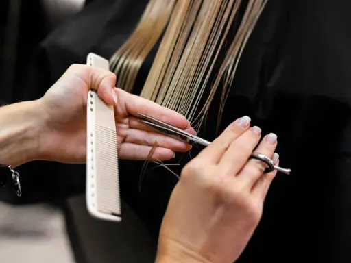 Manos de estilista cortando cabello rubio con tijeras y peine. Decisión: cortar el pelo en seco o mojado.