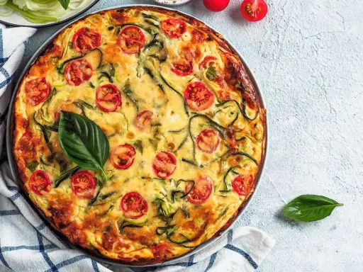 Torta salata vegana con zucchine e pomodorini, guarnita con basilico fresco.