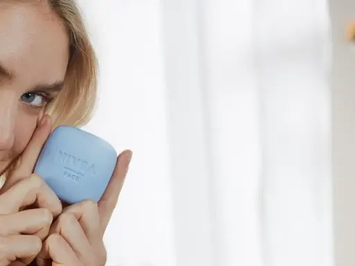 Une femme blonde tient un pain de savon bleu Nivea Face. Elle sourit, sa peau semble douce. Ce savon a un pH neutre, combien est-il doux pour votre visage ?