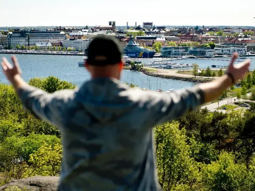 En person med armarna utsträckta njuter av utsikten över en hamn och stad, kanske den soligaste staden i Sverige.
