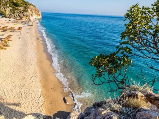 Piękna plaża w Albanii z turkusową wodą i rzędami parasoli. Ceny wakacji w Albanii są przystępne, a widoki zachwycające.