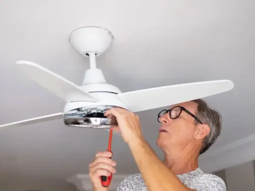 Hombre con gafas ajusta un ventilador de techo pladur con un destornillador.