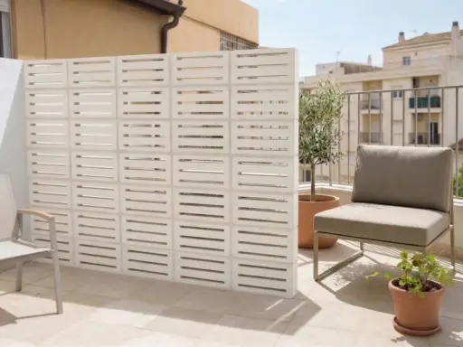 Muros cortina de bloques blancos con diseño de listones horizontales, creando un espacio exterior moderno con silla y plantas.