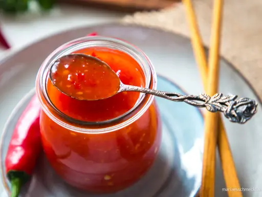 Ein Löffel mit leuchtend roter Thai Chilli Sauce, daneben frische Chilis und Stäbchen.