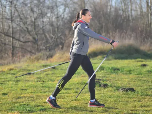 Kobieta w stroju sportowym ćwiczy nordic walking, używając kijków. Widać, jakie kije do nordic walking są lekkie i wygodne.
