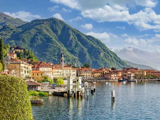 Vista di un paese sul lago d'Iseo, con montagne verdi sullo sfondo. La profondità del lago d'Iseo è suggerita dalla vastità dell'acqua.
