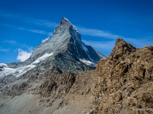 Majestatyczne szwajcaria góry z ośnieżonym szczytem Matterhorn w tle i skalistym zboczem na pierwszym planie.