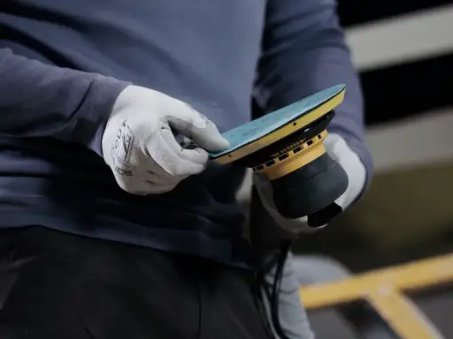 Gants blancs ajustant un disque sur une ponceuse Mirka, prêt à polir la coque d'un bateau.
