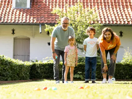Une famille s'amuse dans le jardin avec un jeu de pétanque en ligne. Les boules colorées sont alignées sur l'herbe.