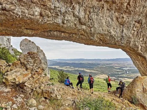 Senderismo Navarra: grupo de excursionistas admira un paisaje montañoso desde debajo de un arco de roca natural.