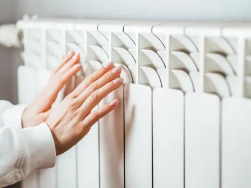 Manos cálidas sobre un convector blanco, sintiendo el calor del invierno.