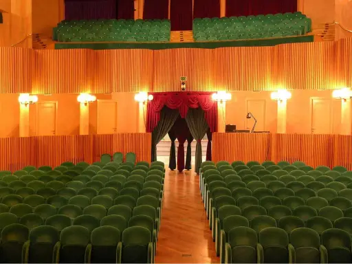 L'arena della regina cattolica, un teatro con poltrone verdi e sipario rosso, attende il pubblico.