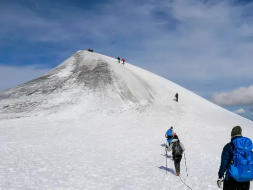 Vandrare klättrar uppför en snöig sluttning mot Kebnekaises topp. En bra packlista för Kebnekaise är avgörande för en säker och njutbar tur.