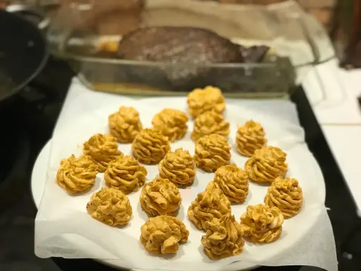 Piped dollops of golden-brown sauce arranged on white parchment paper, with a roasted dish in the background.