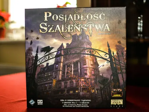 Pudełko gry "Posiadłość Szaleństwa" z mroczną posiadłością i wroną na bramie. Dodatki do tej gry planszowej zapowiadają nowe, przerażające przygody.