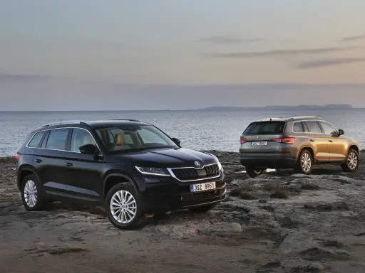 Dwa SUV-y Skoda Kodiaq 2024 na skalistym wybrzeżu. Jeden czarny, drugi w kolorze złota.