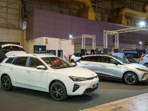 Białe kombi MG5 z otwartą klapą bagażnika i srebrny SUV na wystawie samochodowej.