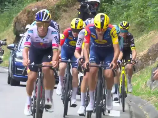 Radsportler im Peloton, darunter Cian Uijtdebroeks, kämpfen sich bergauf. Motorräder und ein Auto begleiten das Rennen.