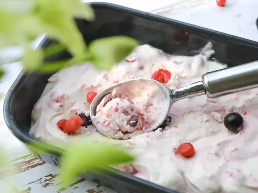 Glace au yaourt italienne aux fruits rouges, servie dans un bac avec une cuillère. Parfait pour une recette facile et rafraîchissante.