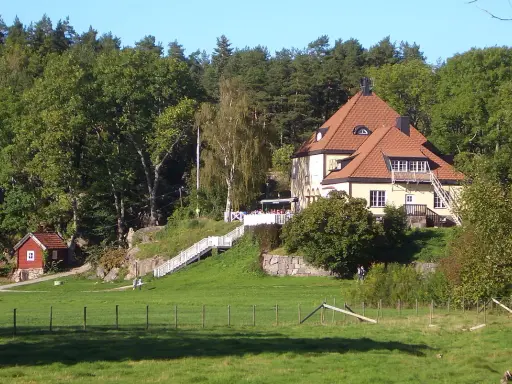 Gula huset vid grinda Stockholm, med röda stugor och grönskande träd.
